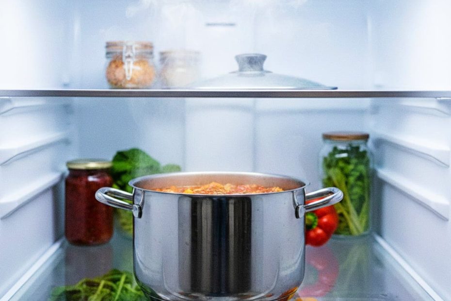 Steaming stainless steel pot with food placed inside a modern clean refrigerator.