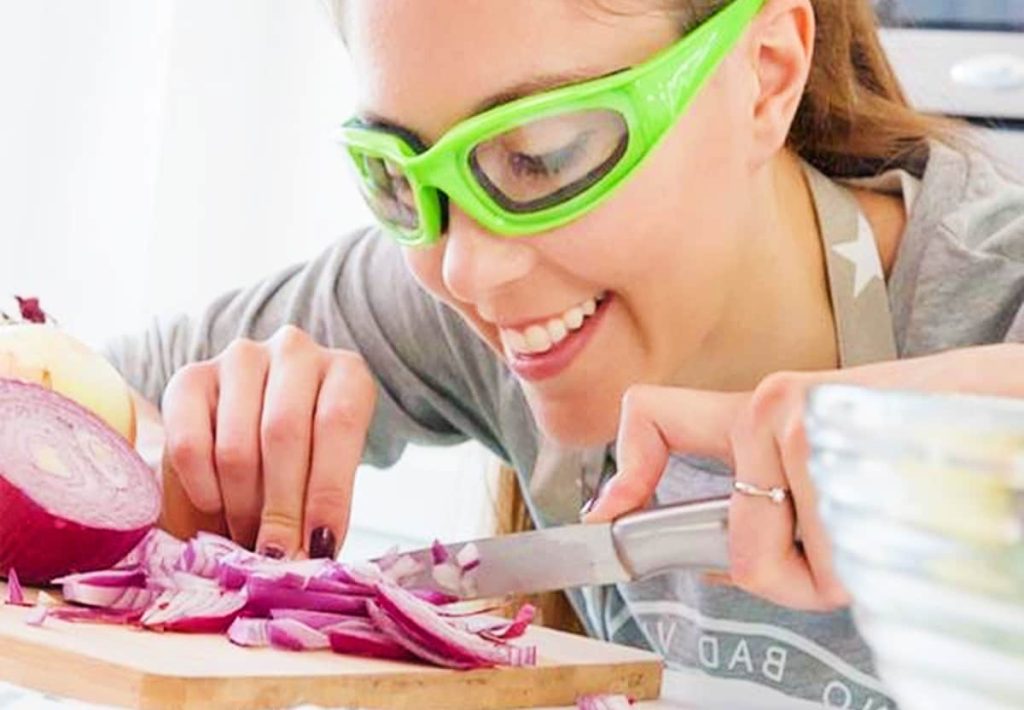 Modern onion goggles sitting on a kitchen counter next to sliced onions, showing eye protection.