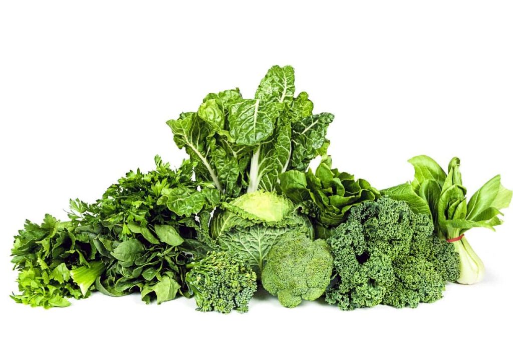 A dense pile of various fresh green vegetables including kale, broccoli, spinach, and bok choy on a white background.
