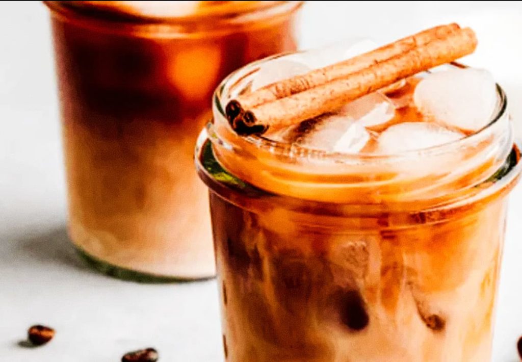 Two glasses of iced coffee with milk and cinnamon sticks on top, showing a creamy texture.