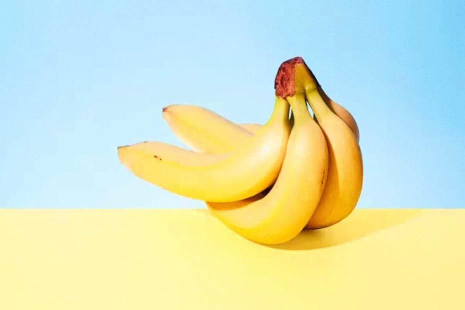 A bunch of five ripe yellow bananas sitting on a yellow surface against a clear light blue background.