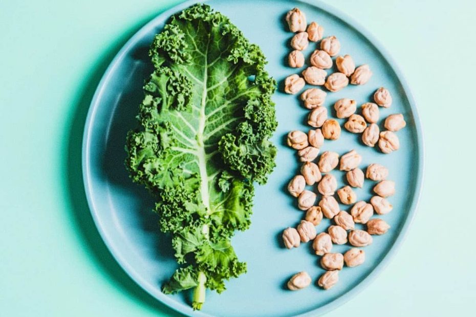 A top-down view of a light blue plate containing a large green kale leaf on the left and a pile of dried chickpeas on the right.