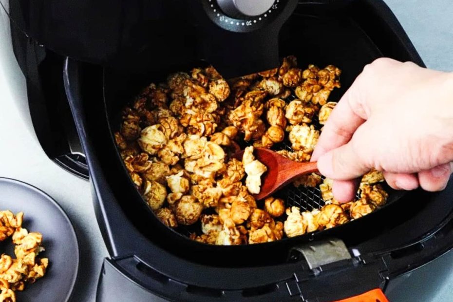 A close-up view of caramel-coated popcorn inside an air fryer basket, with a person's hand using a wooden spoon.