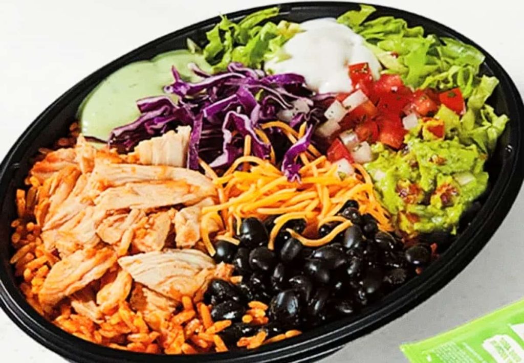 black plastic bowl filled with grilled chicken, black beans, seasoned rice, shredded cheese, purple cabbage, and fresh pico de gallo.