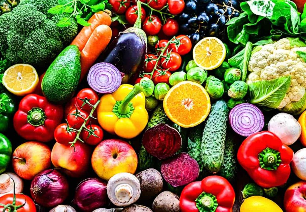 dense and vibrant assortment of various vegetables including broccoli, red peppers, lemons, cucumbers, and leafy greens, showcasing a "rainbow" of nutrients.