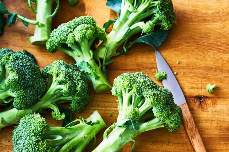 Several fresh green broccoli florets scattered on a wooden cutting board next to a small kitchen knife with a wooden handle.