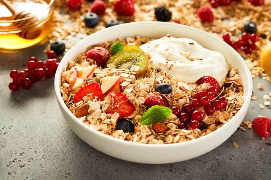 A white bowl filled with rolled oats, topped with Greek yogurt, fresh raspberries, blueberries, kiwi slices, and almonds.