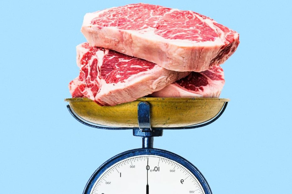 Three raw marbled beef steaks stacked on top of a vintage blue kitchen scale against a light blue background.