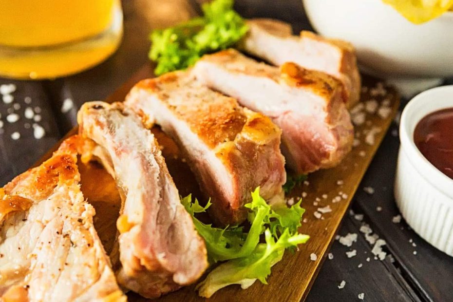 Sliced pork ribs on a wooden board with salt and a side of sauce, representing high-protein sources of serine.