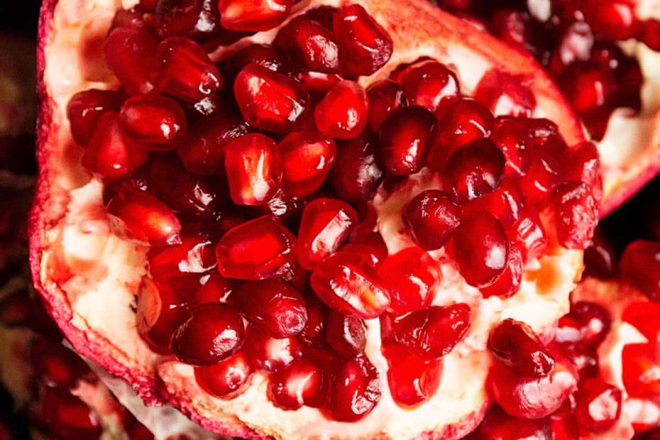 A close-up, top-down shot of a halved pomegranate, revealing the tightly packed, vibrant red arils and white inner membranes.
