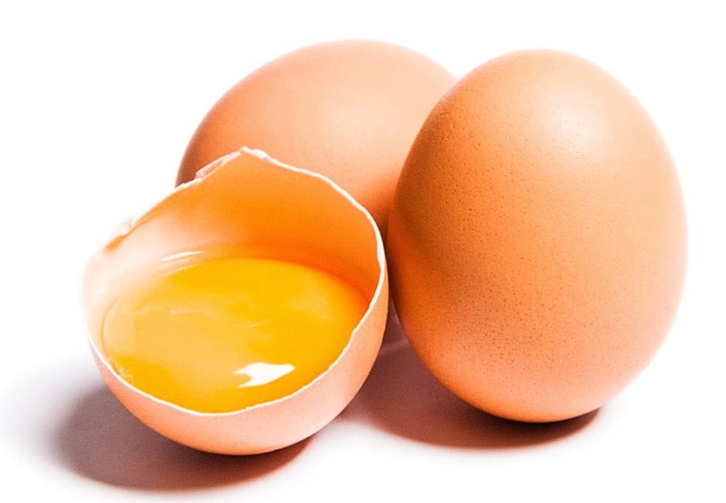 Three brown eggs on a white background, with one cracked open to reveal a bright yellow yolk and clear egg white.