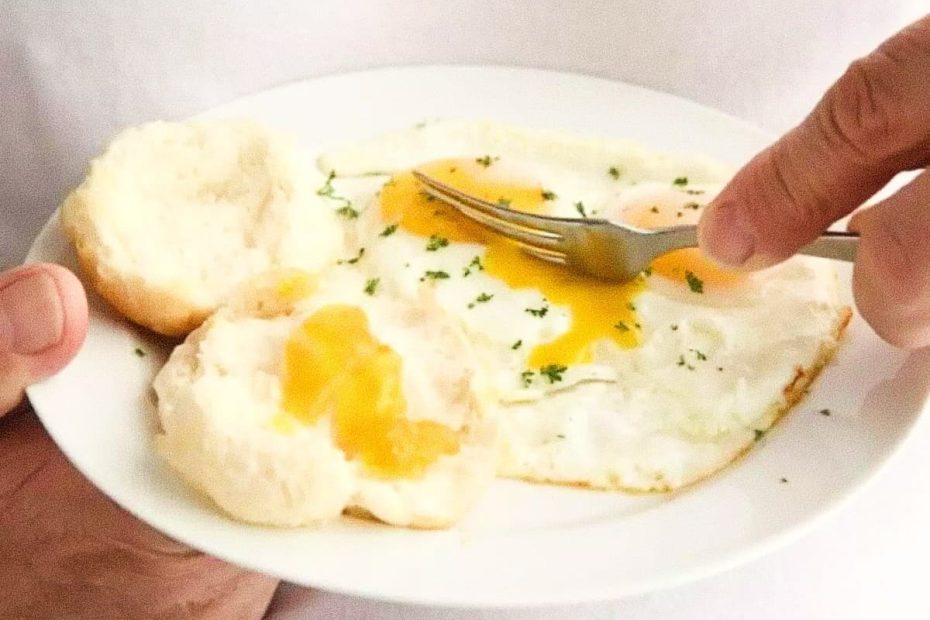 A person holding a white plate with sunny-side-up eggs sprinkled with herbs and two warm biscuits, ready for a post-workout meal.