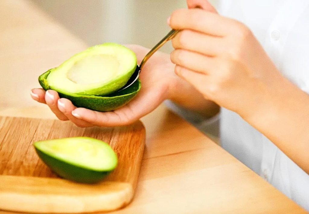 A person scooping a fresh avocado half with a spoon, demonstrating the practical serving size for heart health.