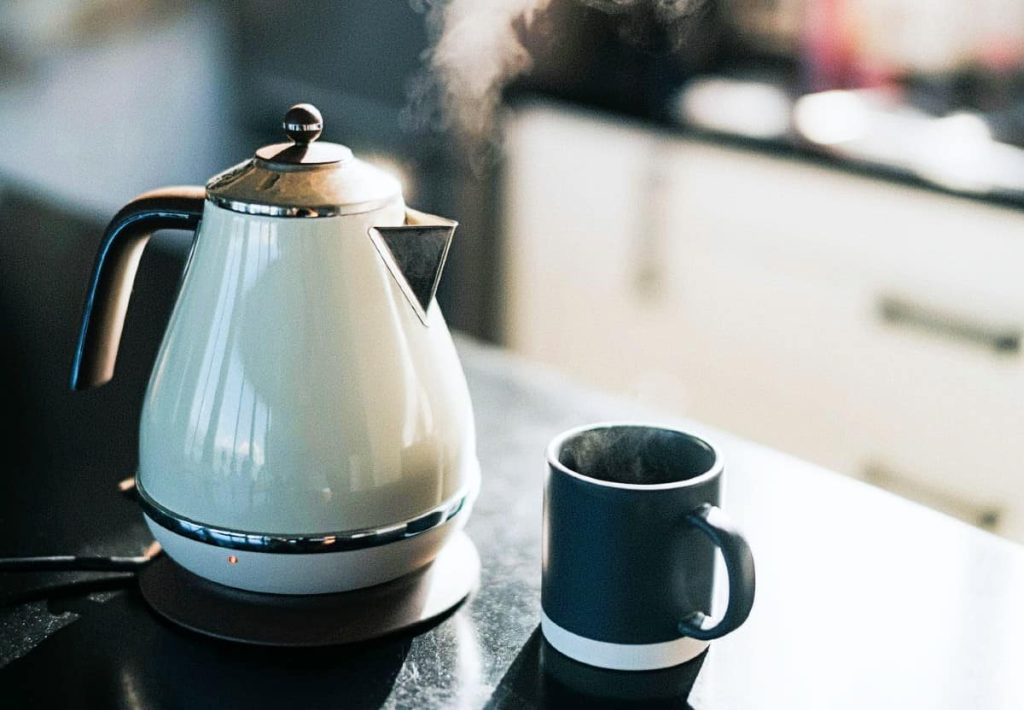 A retro-style electric kettle boiling and steaming on a dark kitchen counter next to a steaming dark mug.