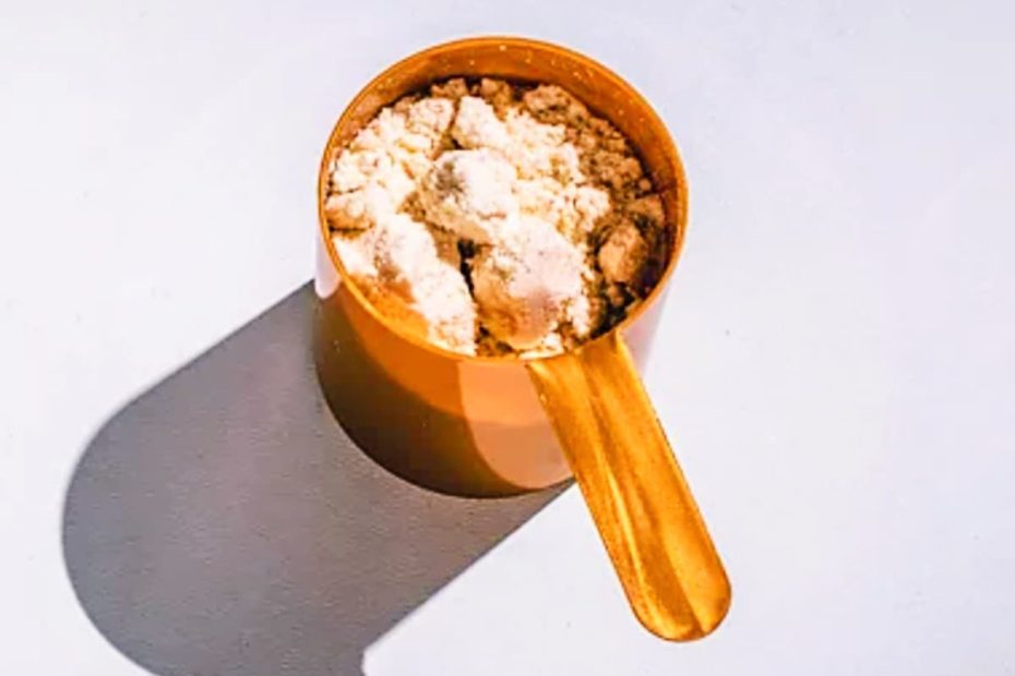 A golden supplement scoop filled with white creatine monohydrate powder casting a sharp shadow on a white surface.