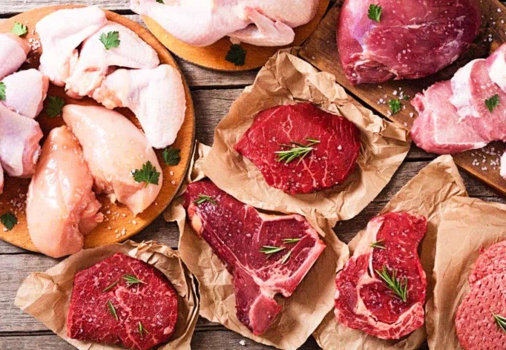 A top-down view of various fresh meat cuts, including chicken breast, beef steaks, and pork, seasoned with rosemary on butcher paper.