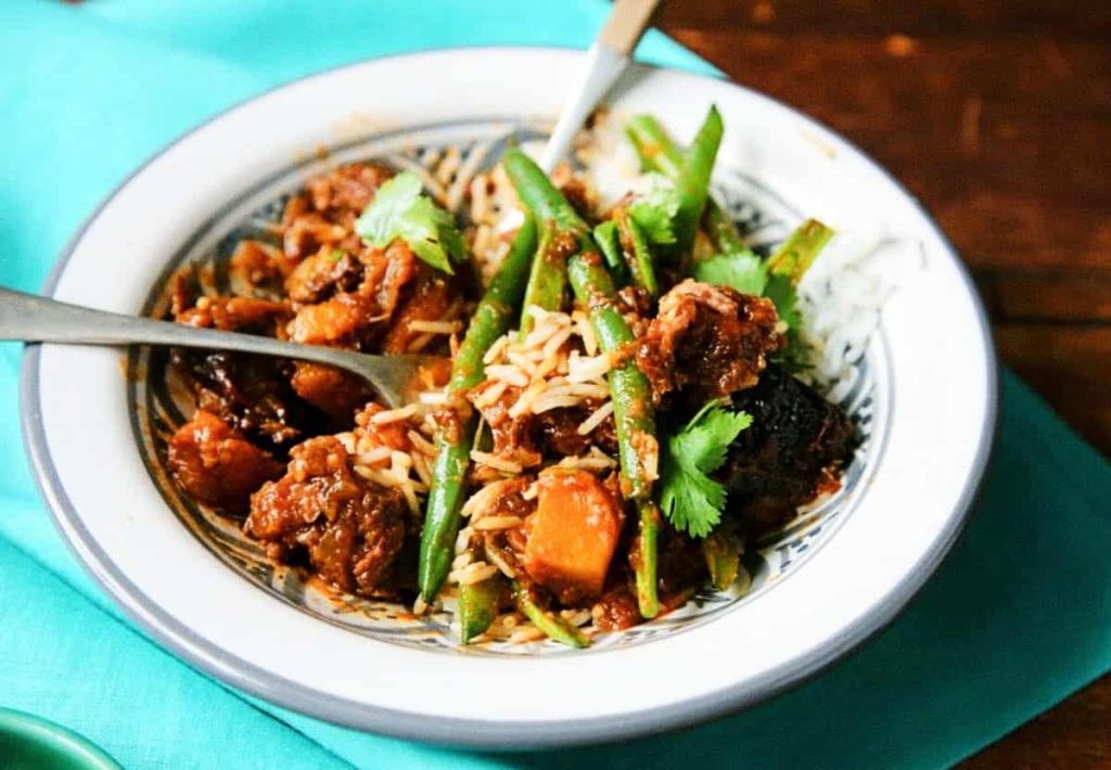A nutritious bowl of goat meat stew with green beans, carrots, and rice, garnished with fresh cilantro.