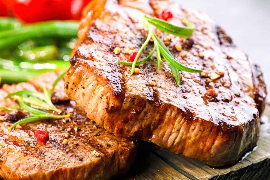 Two juicy, grilled lean beef steaks seasoned with rosemary and peppercorns on a wooden board.