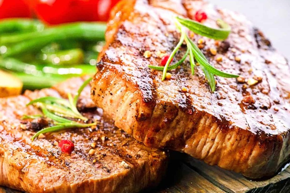 Two juicy grilled lean steaks seasoned with rosemary and peppercorns, served with green beans in the background.