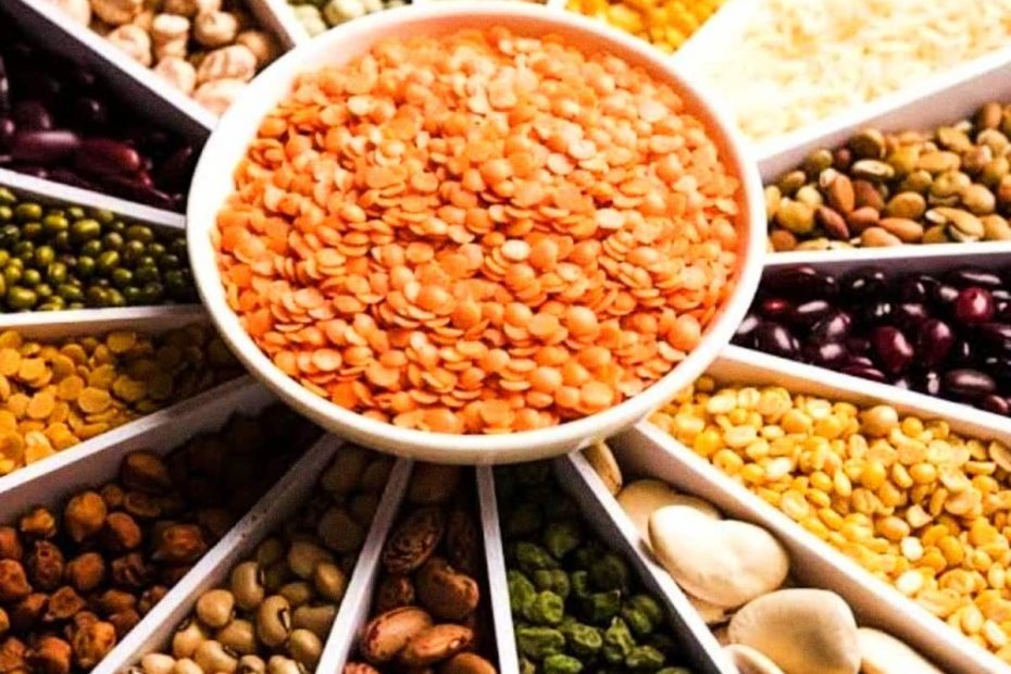 A central bowl of red lentils surrounded by various types of beans and chickpeas in a radial arrangement.