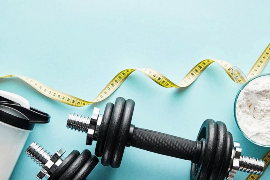 Flat lay of adjustable dumbbells, a measuring tape, a shaker bottle, and a scoop of white powder on a light blue background.
