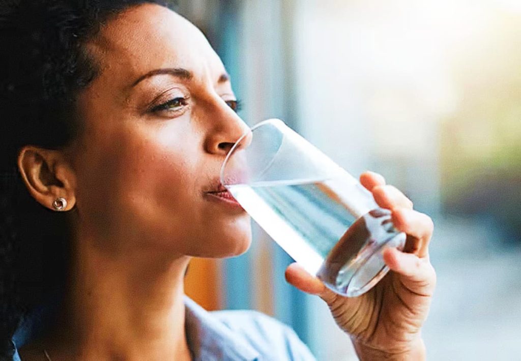 A woman drinking water from a glass in a bright environment, focusing on metabolic health.