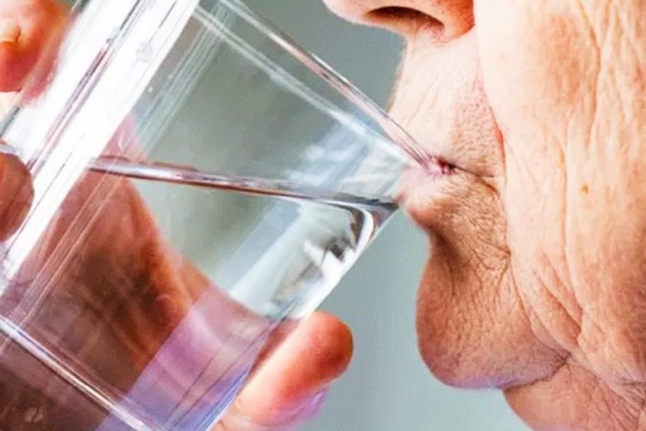 A close-up side view of an elderly person drinking water from a clear glass.