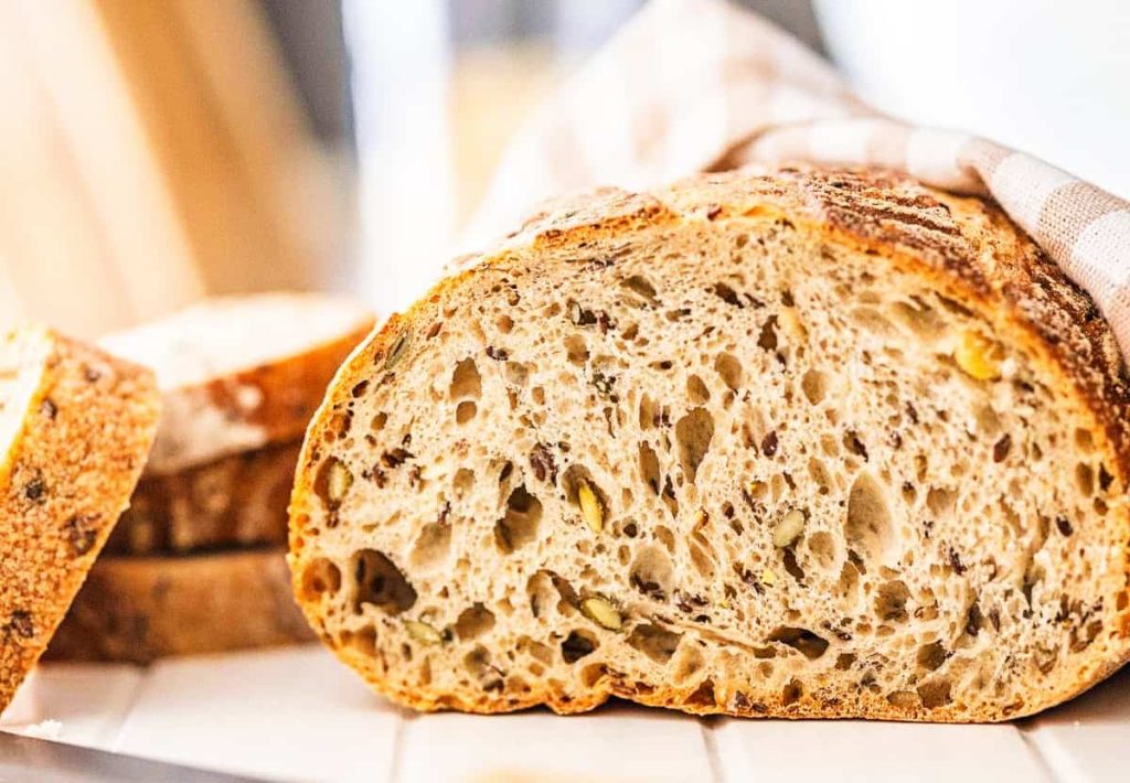 A close-up cross-section of a seeded sourdough bread loaf, showing the fiber-rich grains and fermented airy texture.